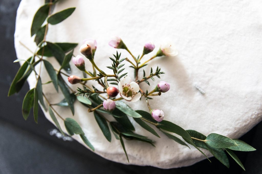 Blumendekoration mit rosa und weißen Knospen mit grünen Blättern auf rundem Kuchen aus Vogelperspektive.